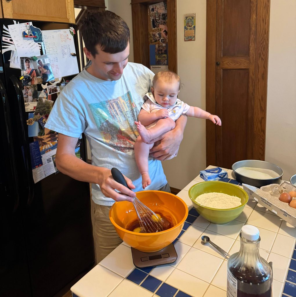 A Dad, baking Maple Cake while holding a baby.
