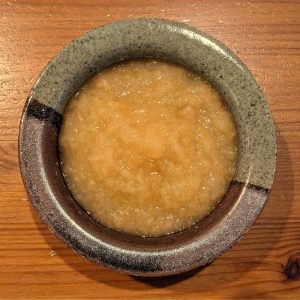 A top-down view of golden-brown homemade applesauce in a ceramic bowl.
